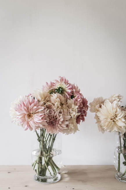 Mesa de madeira com buquês de flores frescas em vasos perto da parede branca — Fotografia de Stock