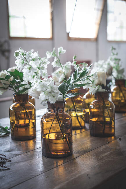 Set of light bloom branches in retro glass vases with water on wooden table in room — Stock Photo