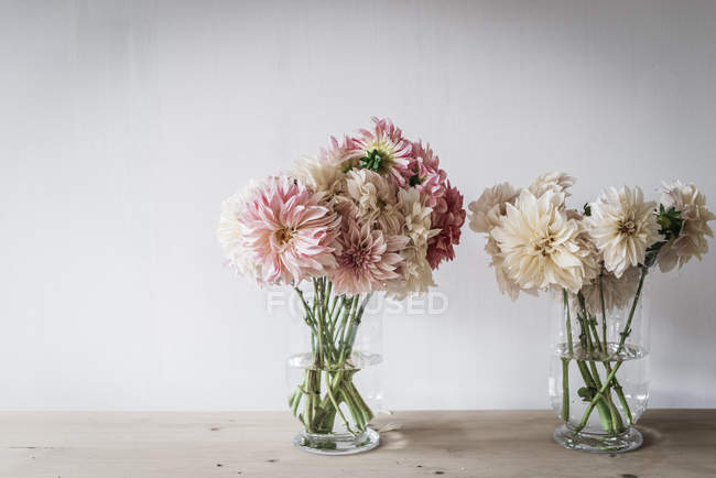 Holztisch mit Sträußen frischer Blüten in Vasen in der Nähe der weißen Wand — Stockfoto