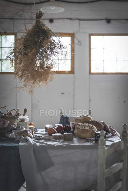 Bunch of dry coniferous twigs hanging on twist above table with bakery near chairs in room — Stock Photo