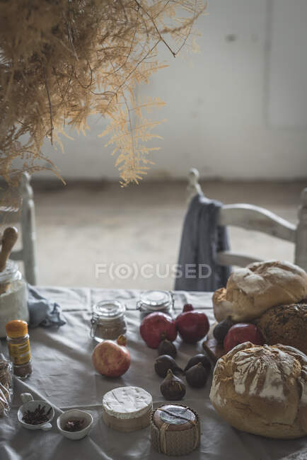 Ramo de ramitas de coníferas secas colgando de la torcedura sobre la mesa con panadería cerca de sillas en la habitación - foto de stock