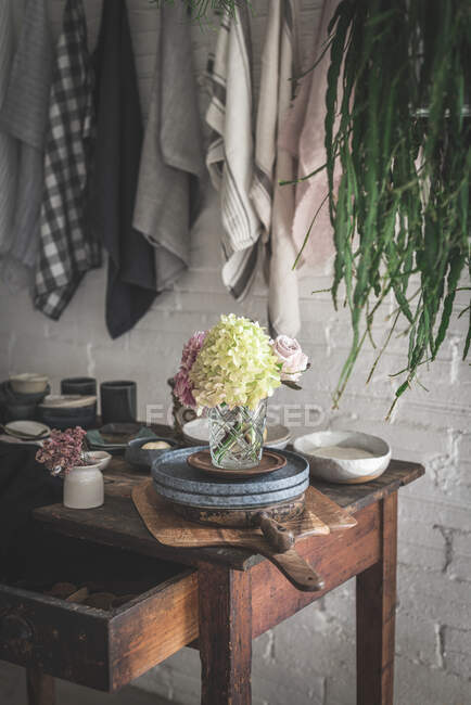 Table en bois avec bouquet de chrysanthèmes roses frais et hortensia blanche dans un vase entre poêle et ustensiles de cuisine près de torchons suspendus à l'aide d'épingles — Photo de stock