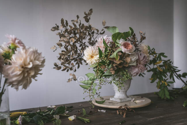 Concepto de ramo de rosas secas y frescas, crisantemos y ramitas de plantas en jarrón retro sobre tabla de madera sobre fondo gris - foto de stock