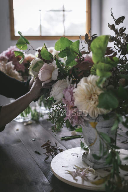 Frau macht Bouquet aus trockenen und frischen Rosen, Chrysanthemen und Pflanzenzweigen in Retro-Vase auf Holzbrett auf grauem Hintergrund — Stockfoto