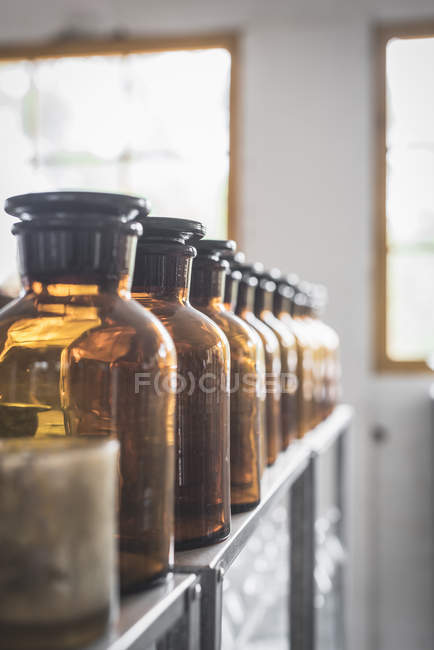 Fila de frascos de vidro retro colocados na prateleira no quarto no fundo embaçado — Fotografia de Stock
