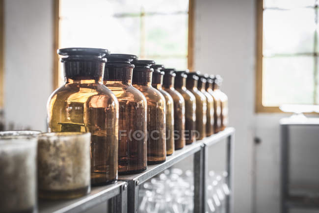 Fila de frascos de vidro retro colocados na prateleira no quarto no fundo embaçado — Fotografia de Stock