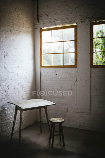 Konzept von Tisch in der Nähe von Hocker in grauen Raum mit gemauerten Wänden — Stockfoto
