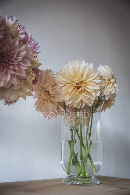 Wooden table with kitchenware and bouquets of fresh blooms in vases with water near white wall — Stock Photo