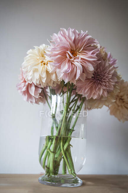 Дерев'яний стіл з посудом і букетом свіжих квітів у вазі з водою біля білої стіни — стокове фото