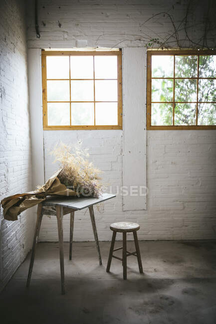Conceito de buquê de galhos de coníferas secos em papel artesanal na mesa perto de banquinho em quarto cinza escuro com paredes de tijolo — Fotografia de Stock