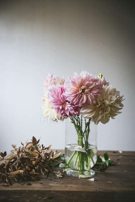 Tavolo in legno con stoviglie e mazzo di fiori freschi in vaso con acqua vicino alla parete bianca — Foto stock