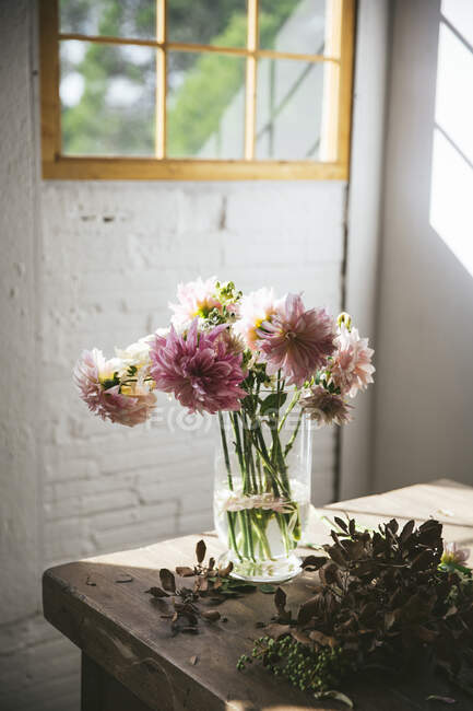 Деревянный стол с кухонными принадлежностями и букетами свежих цветов в вазах с водой возле белой стены — стоковое фото