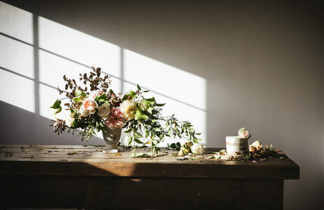 Prato com saboroso bolo decorado botão flor na mesa de madeira com cacho de crisântemos, rosas e galhos de plantas em vaso entre folhas secas sobre fundo cinza — Fotografia de Stock