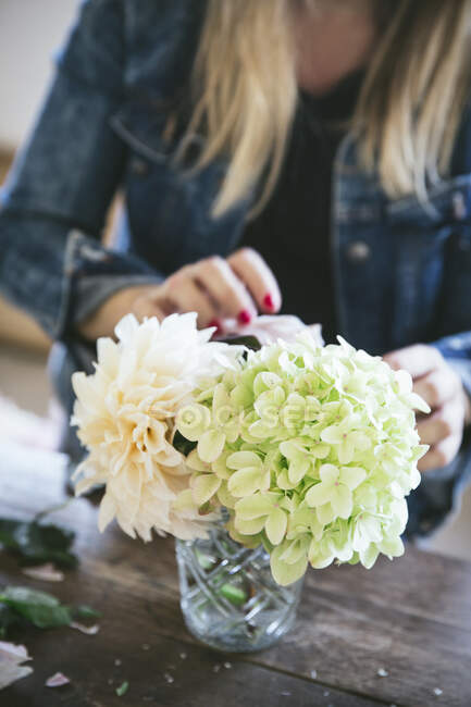 Felice signora vicino al tavolo di legno con mazzi di crisantemi freschi, rose e ramoscelli di piante in vasi su sfondo grigio — Foto stock