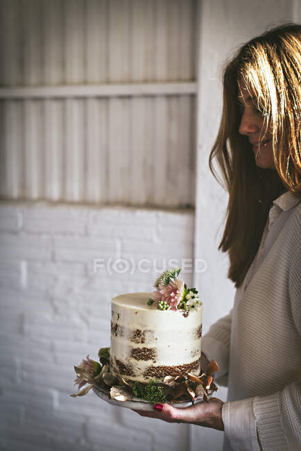 Smiling woman holding plate with cake decorated by flowers and p — Stock Photo
