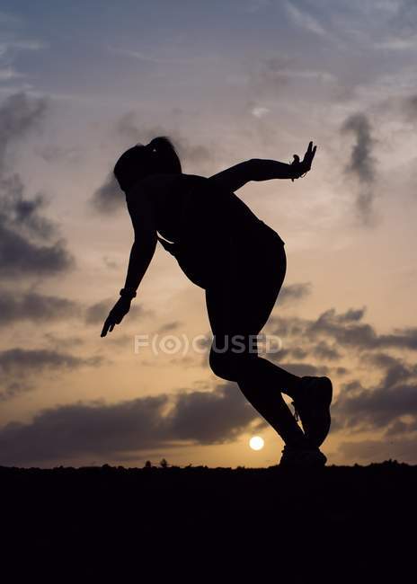 Силует стрибаючої жінки на фоні заходу сонця — стокове фото