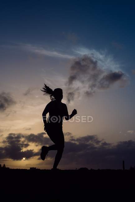 Silhouette de jogging femme sur fond de coucher de soleil ciel — Photo de stock
