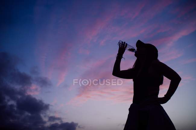 Silhouette della donna che beve acqua sullo sfondo del cielo del tramonto — Foto stock