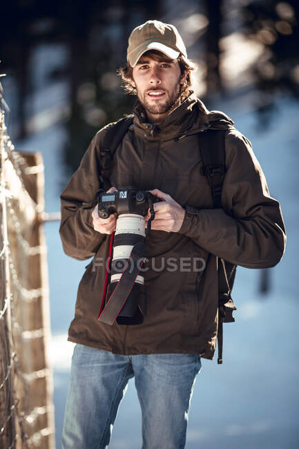 Young photographer with professional camera looking at camera between winter forest in Cerdanya, France — Stock Photo