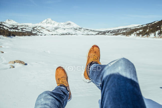 Ковток чоловічих ніг у джинсах і зимових чоботах, сидячи на снігу в сонячний день біля пагорбів Серданья, Франція. — стокове фото