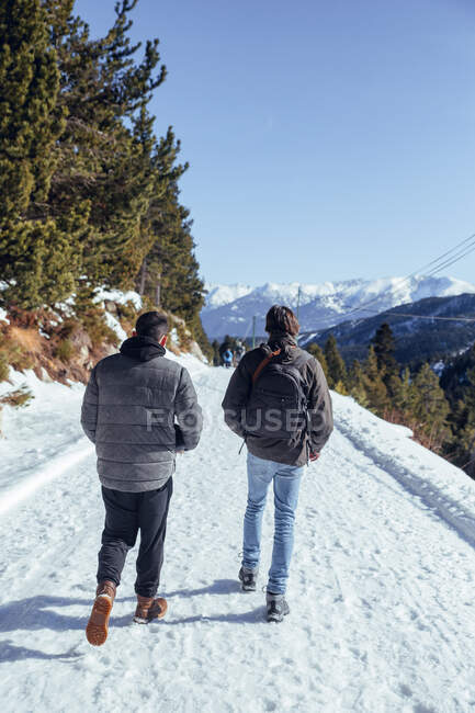 Back view of males walking on countryside walkway between mountains in snow in Cerdanya, France — Stock Photo