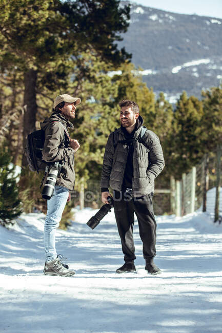 Jovens fotógrafos com câmeras profissionais conversando entre árvores verdes e neve em Cerdanya, França — Fotografia de Stock