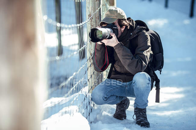 Молодой фотограф снимает на профессиональную камеру рядом с забором между снегом зимой в Серданье, Франция — стоковое фото