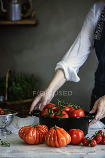 Senhora colheita segurando pote com tomates frescos vermelhos na mesa — Fotografia de Stock