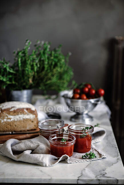 Delizioso pane di segale aromatico fresco sul tovagliolo vicino a coltello e lattine con marmellata fatta in casa di pomodori su sfondo sfocato — Foto stock
