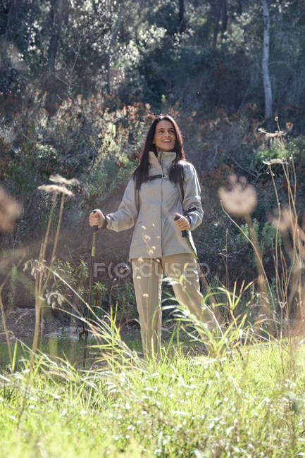Glückliche Frau mit Trekkingstöcken im Wald — Stockfoto