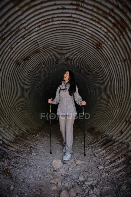 Femme heureuse avec des bâtons de trekking dans le tunnel sombre — Photo de stock