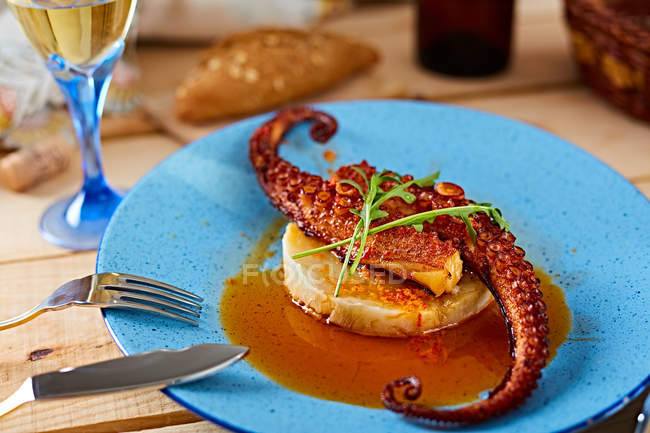 Grilled octopus served with sauce on polenta on blue plate on wooden table — Stock Photo