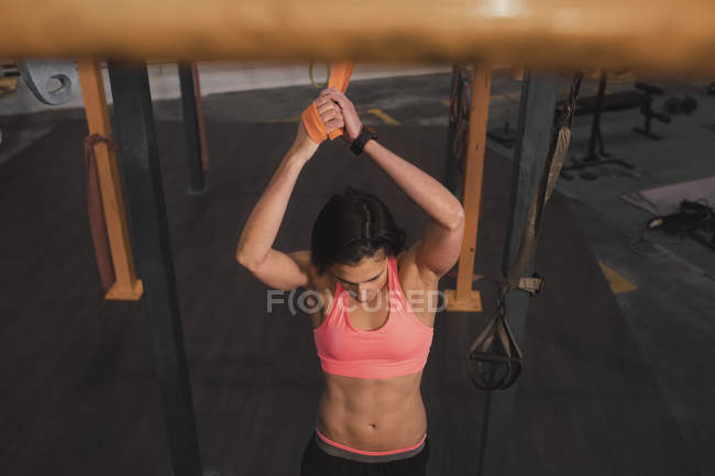 Joven mujer deportiva delgada en ropa deportiva haciendo ejercicios de pull up en la barra horizontal en el gimnasio - foto de stock