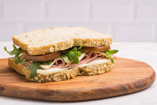 Delicious sandwich with ham, cheese and greens on wooden chopping board — Stock Photo