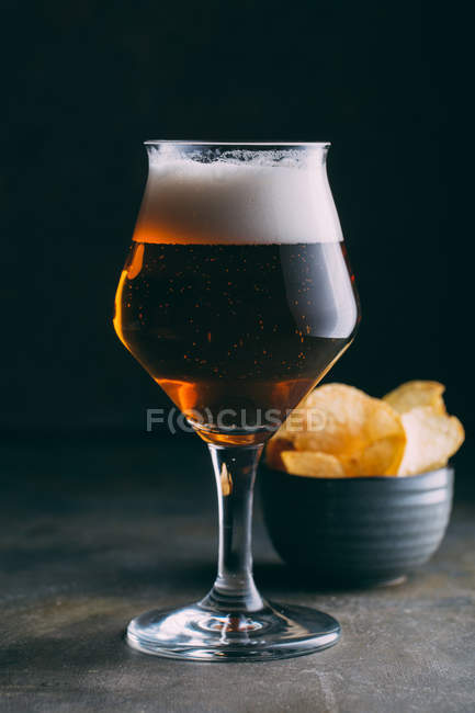 Verre de bière et chips sur fond sombre grunge — Photo de stock