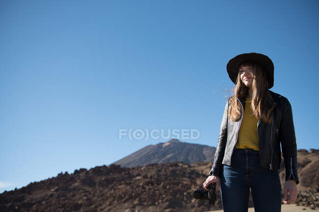 Женщина-фотограф стоит с камерой и смотрит на холмы в пустыне — стоковое фото