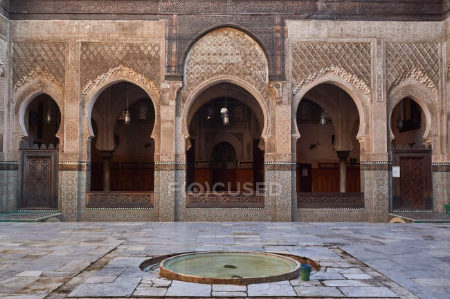 Gran contenedor con agua entre la calle cerca de la fachada del antiguo edificio de piedra con puertas vintage en Marrakech, Marruecos - foto de stock