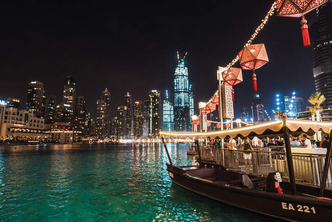 Bella barca e molo affollato vicino acqua increspata a notte incredibile nella città illuminata di Dubai — Foto stock