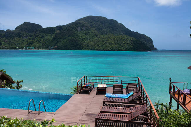 Terraza con tumbonas y piscina azul en laguna turquesa cerca del océano - foto de stock