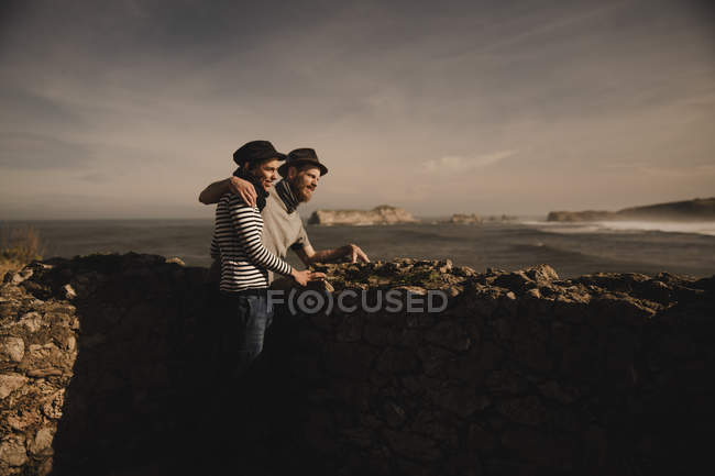 Vue latérale d'élégant couple élégant près des rochers sur la côte près de la mer et le ciel merveilleux — Photo de stock