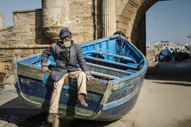 Essaouira, Marruecos, 31 de diciembre de 2017: Marinero con barba sentado en barco en el puerto - foto de stock