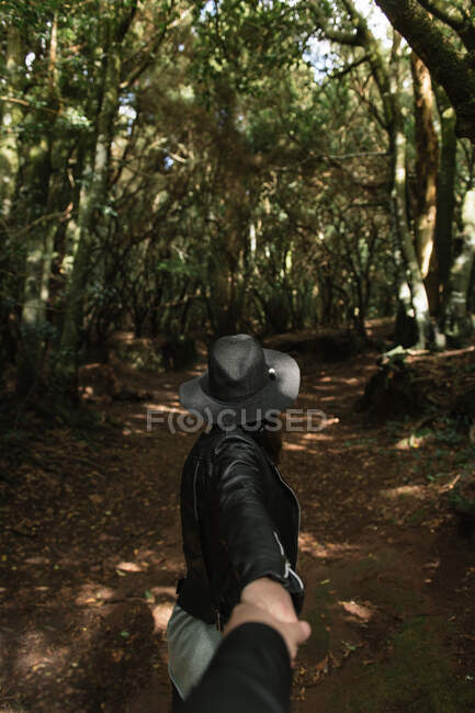 Seitenansicht einer eleganten Dame mit Hut und Lederjacke, die die Hand einer Person hält und auf einem Fußweg zwischen trüben Gassen hoher Mauern und Wäldern steht — Stockfoto