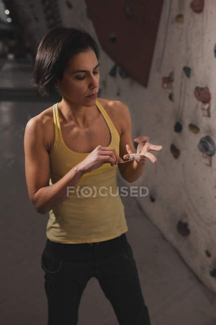 Woman in sportswear fixing finger tape near wall with climbing holds in gym — Stock Photo