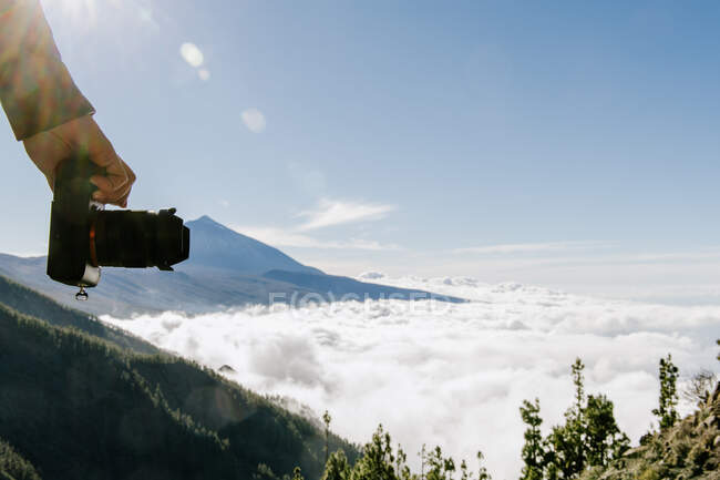 Mão de colheita de fotógrafa feminina em pé no topo da colina segurando câmera em dia ensolarado cloudscape — Fotografia de Stock