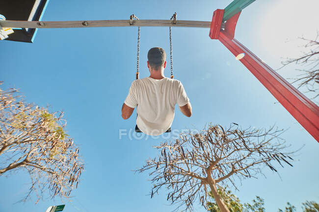 Man swinging on playground in sunlight — Stock Photo