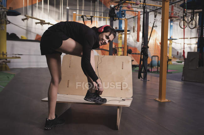 Vista lateral de mujer en ropa deportiva con auriculares escuchando música y zapato de cordones en gimnasio - foto de stock