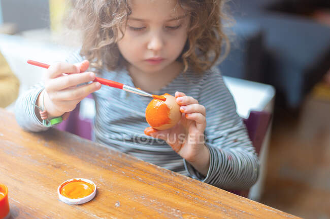 Toddler girl painting egg at table — Stock Photo