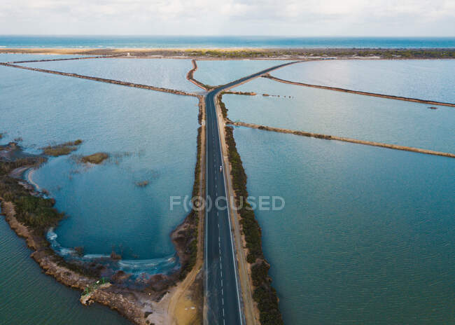 Carretera de asfalto vacía entre arroyos de color turquesa a orillas del mar - foto de stock
