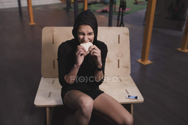 Mujer joven en ropa deportiva con pasteles de arroz de energía sentado en el banco en el gimnasio - foto de stock