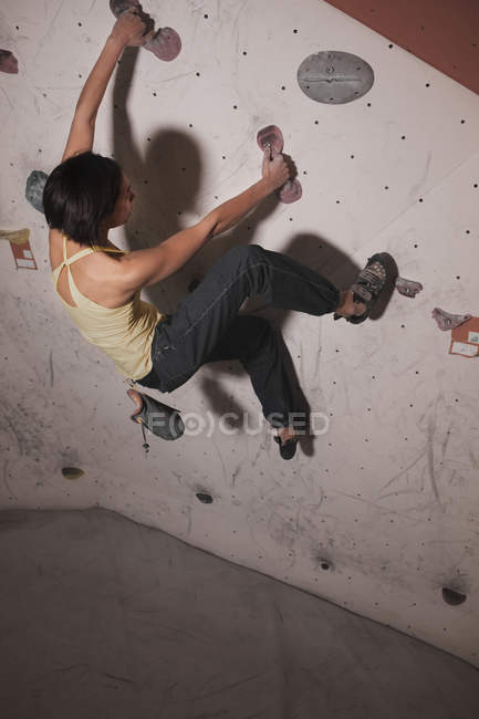 Visão traseira da mulher no treinamento de sportswear na parede de escalada com porões no ginásio — Fotografia de Stock